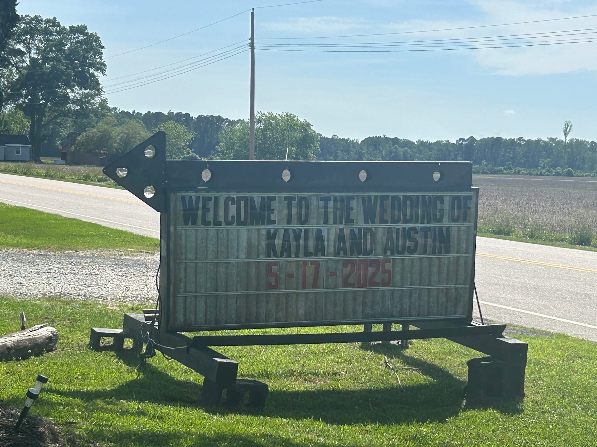 Roadside marquee sign reading Welcome to the Wedding of Kayla and Austin 5-17-2025 on the grounds of a rural estate venue.