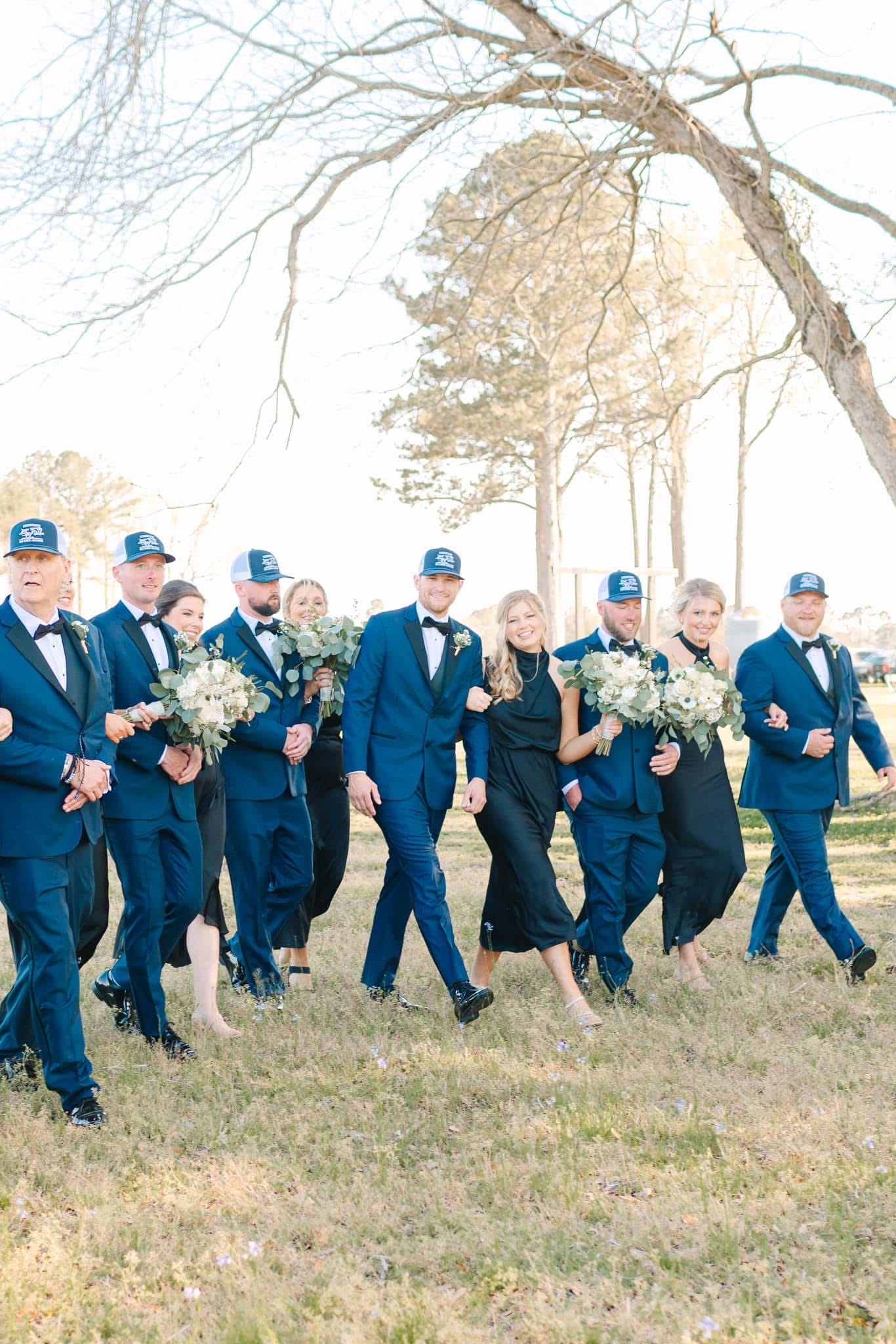 Wedding party in navy tuxedos and black gowns walking and laughing together across the open grounds at Scarborough House estate.