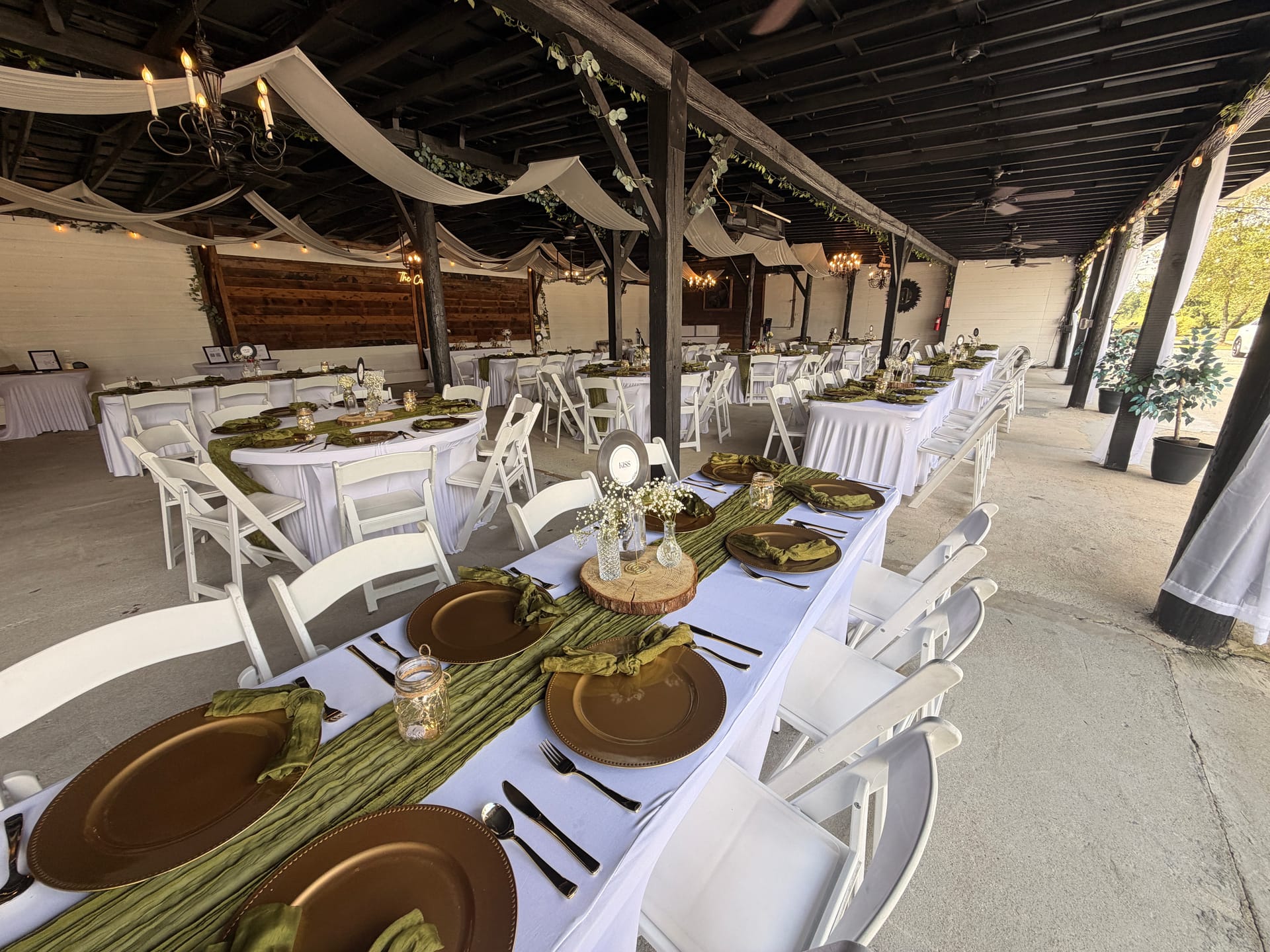 Elegantly styled wedding reception tables with white linens, copper charger plates, sage green runners, and baby's breath centerpieces beneath white fabric draping in the Scarborough House magnolia pavilion.