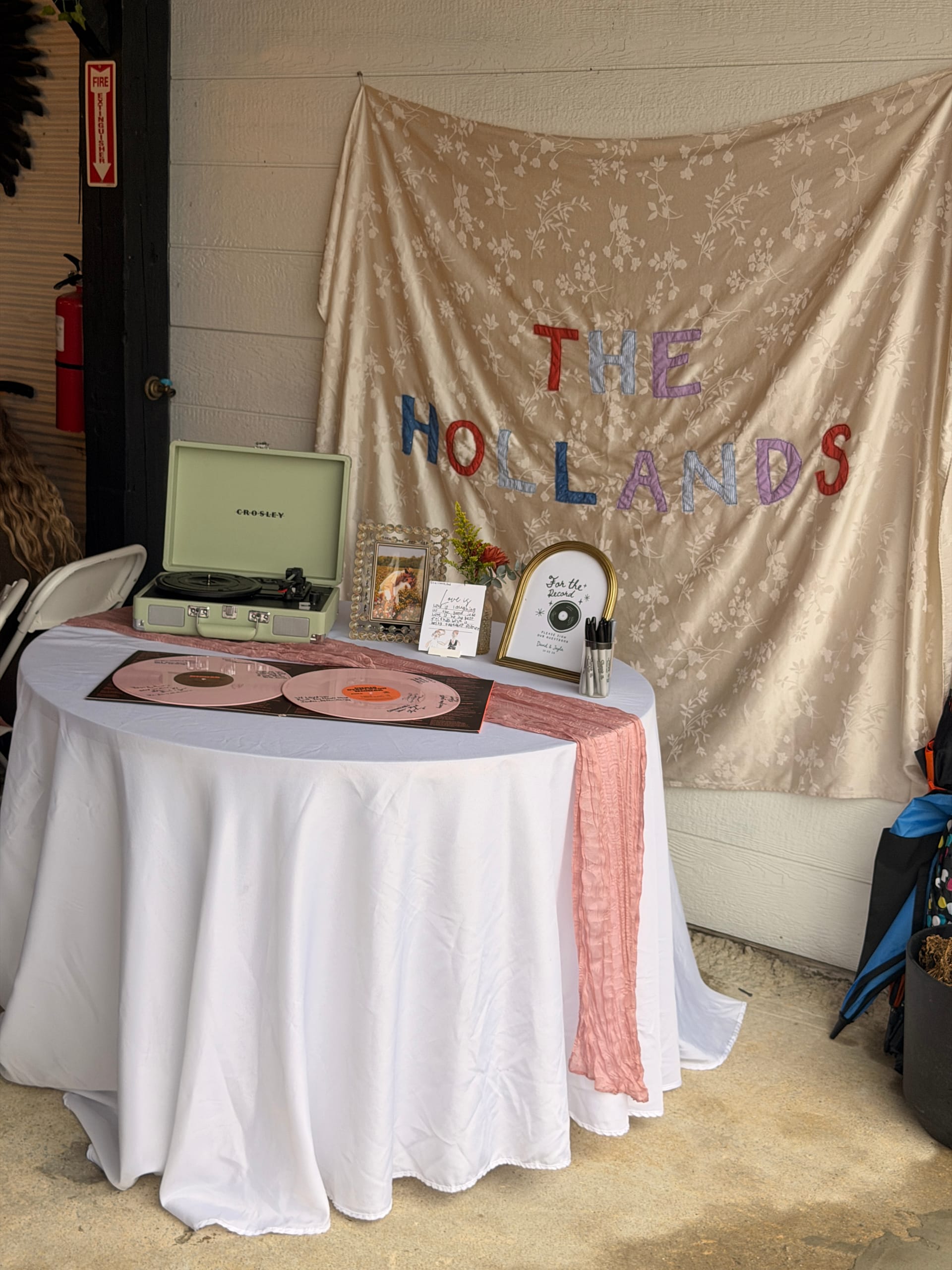 A styled wedding guest book table featuring pink vinyl records, a Crosley turntable, and a floral fabric backdrop reading The Hollands at Scarborough House.