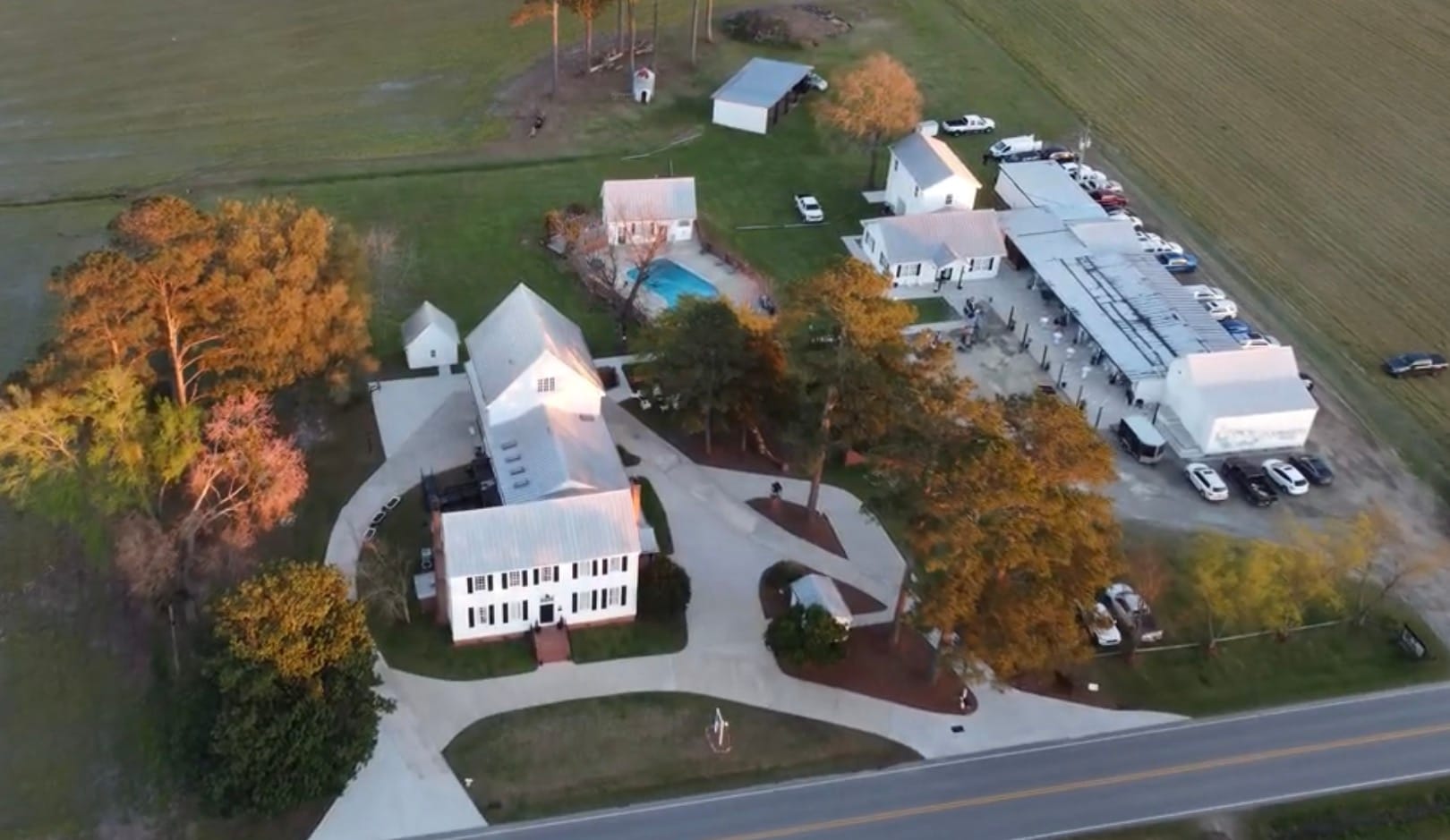 Aerial drone view of Scarborough House historic estate wedding venue showing the 1821 white manor house, pool, oak trees, outbuildings, and surrounding farmland fields at golden hour.