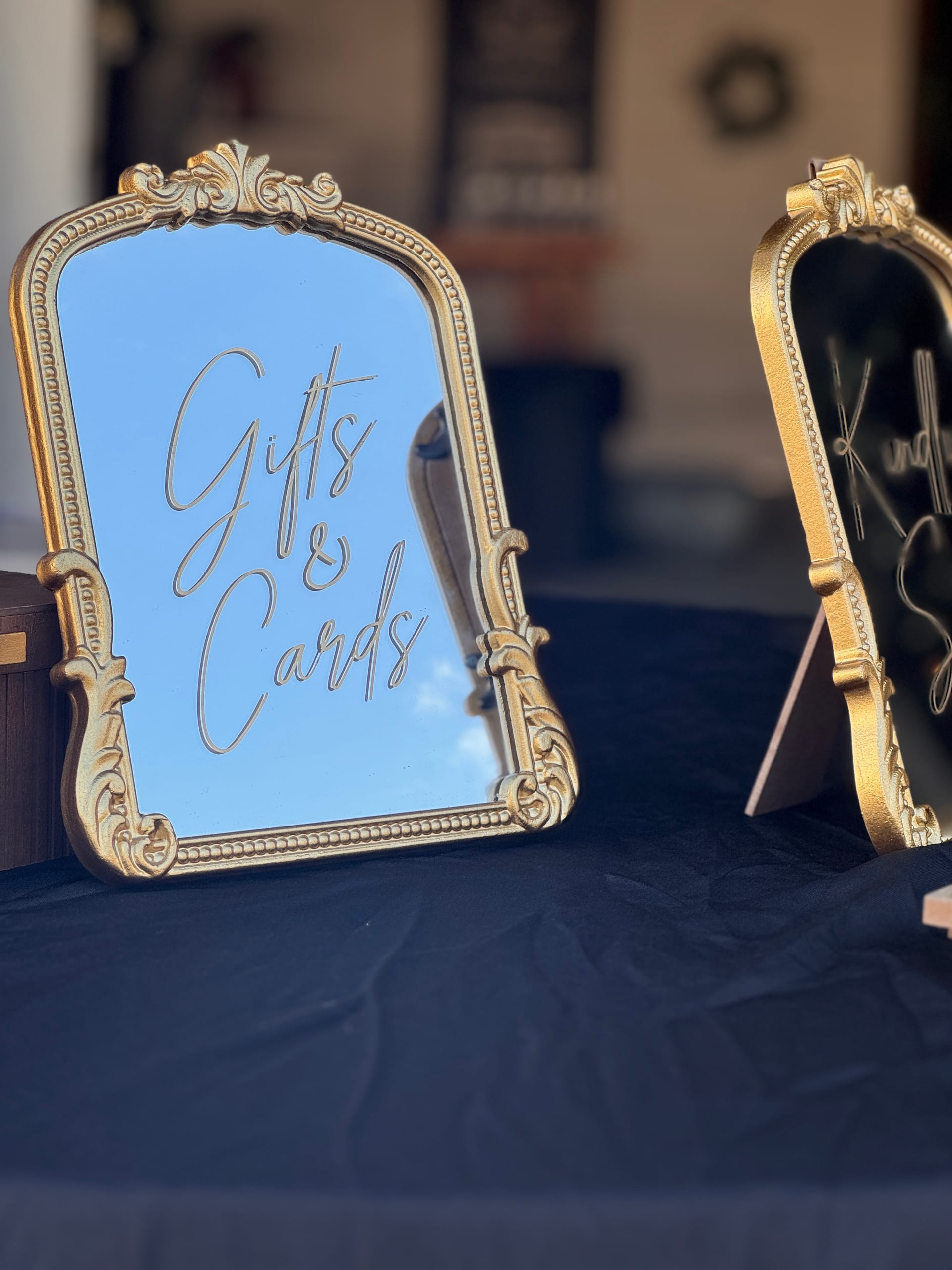 An ornate gold-framed mirror sign with cursive Gifts and Cards calligraphy displayed on a black-draped table at a wedding reception.