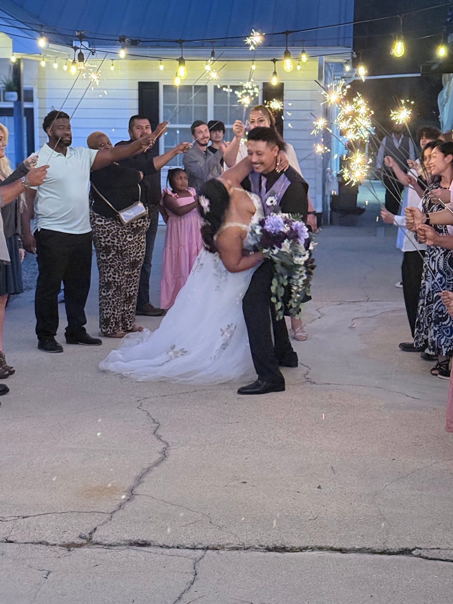 Bride and groom share a romantic dip kiss during a sparkler exit surrounded by cheering wedding guests under string lights at Scarborough House.
