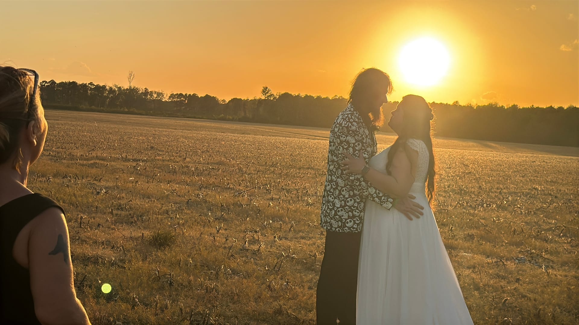 Bride in white gown and groom in patterned shirt embrace face-to-face in golden-hour sunlight over open farmland fields at Scarborough House historic estate wedding venue.