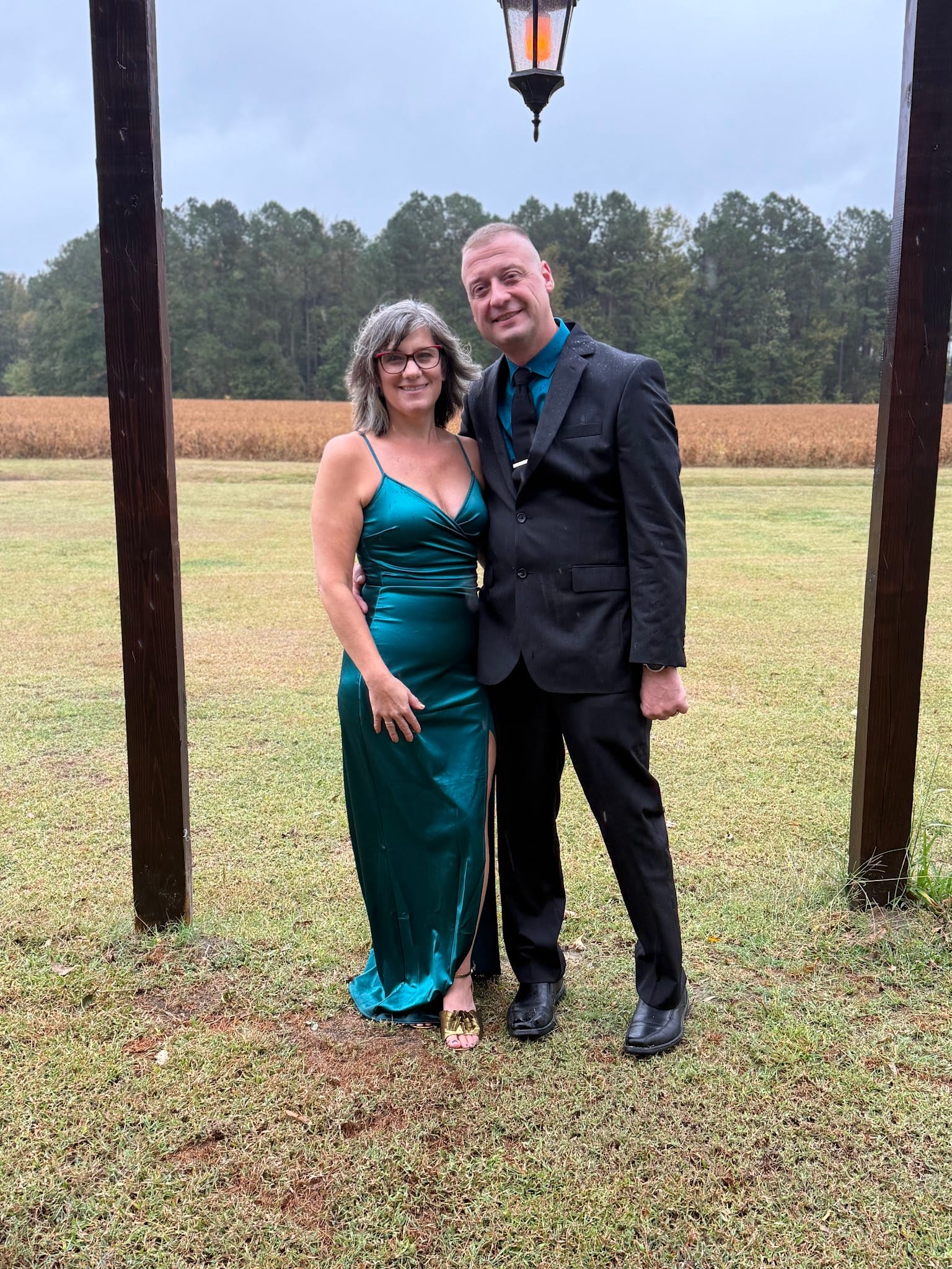 Elegantly dressed couple posing under a lantern post with sweeping farmland fields and tree line in the background at Scarborough House wedding venue.