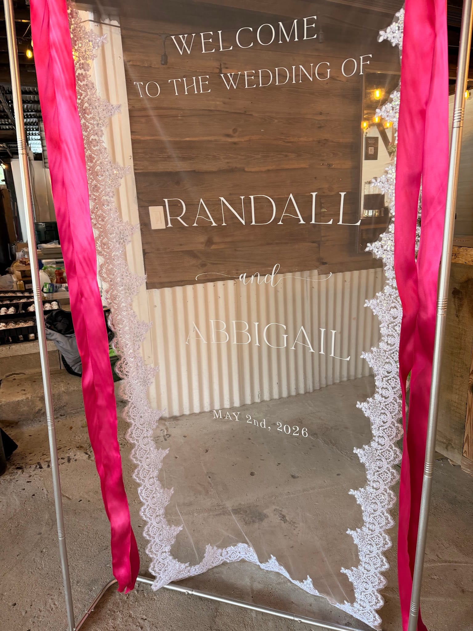 Acrylic wedding welcome sign with lace border and hot pink ribbon streamers announcing the marriage of Randall and Abbigail on May 2nd 2026.
