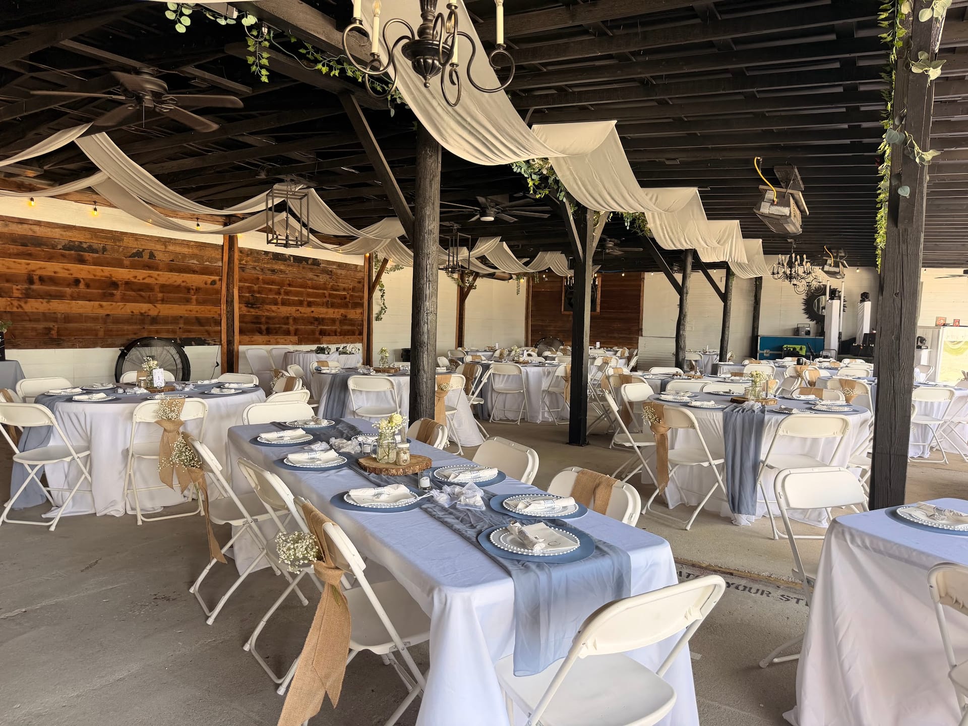 Elegantly styled open-air pavilion reception space at Scarborough House featuring white draping, chandeliers, blue table runners, and rustic wooden accents set for a wedding celebration.