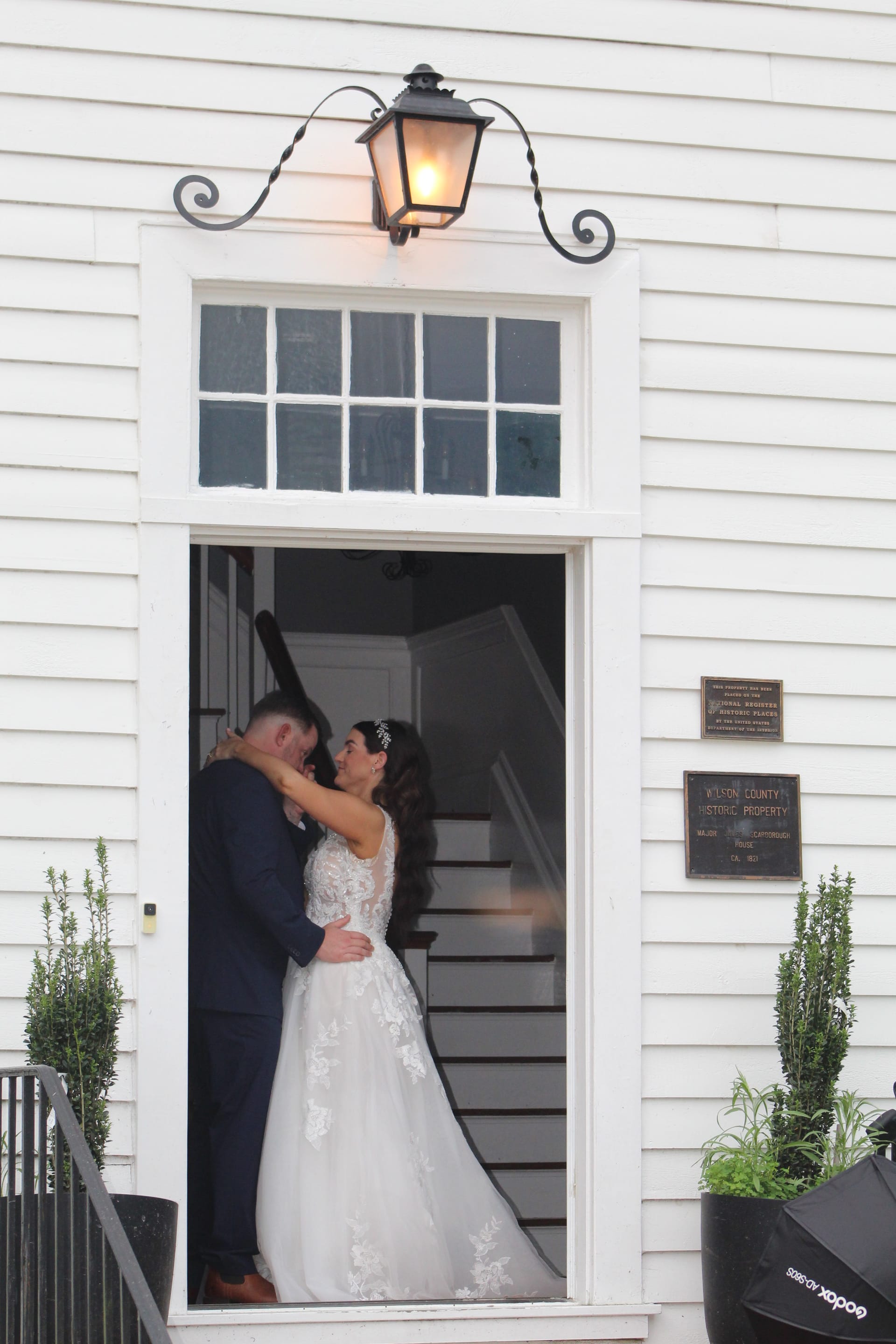 Bride in a lace ballgown and groom in a navy suit share a tender embrace in the illuminated Scarborough House doorway.