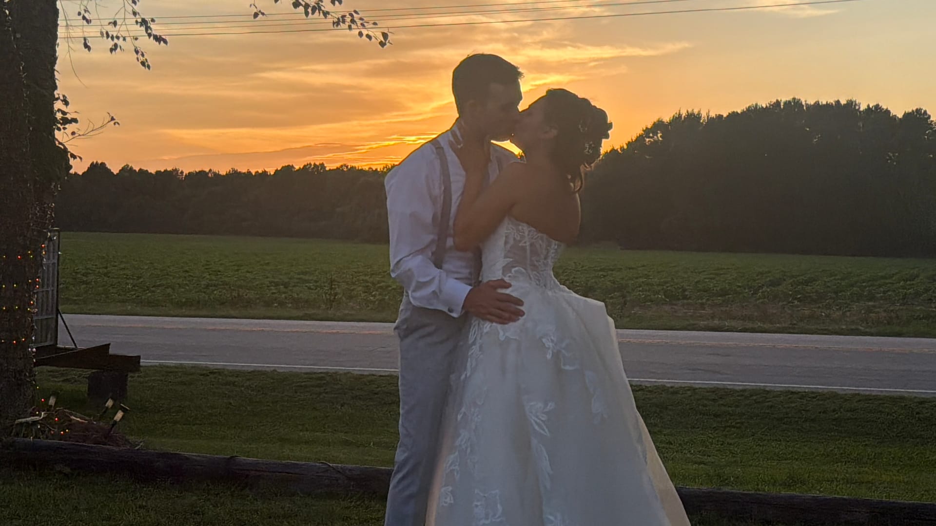 Bride and groom share a romantic kiss silhouetted against a vibrant golden sunset over open farmland fields at Scarborough House estate.