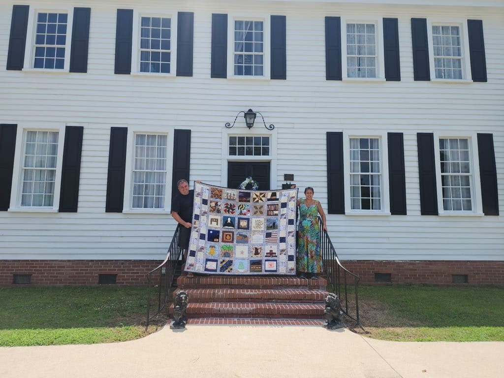 Two friends hold the patriotic 250th anniversary quilt on the brick steps of Scarborough House near Wilson, NC