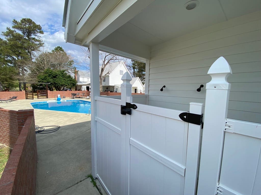 White fence and self-latching gate enclosing the Scarborough House pool, with the pool and deck visible beyond.