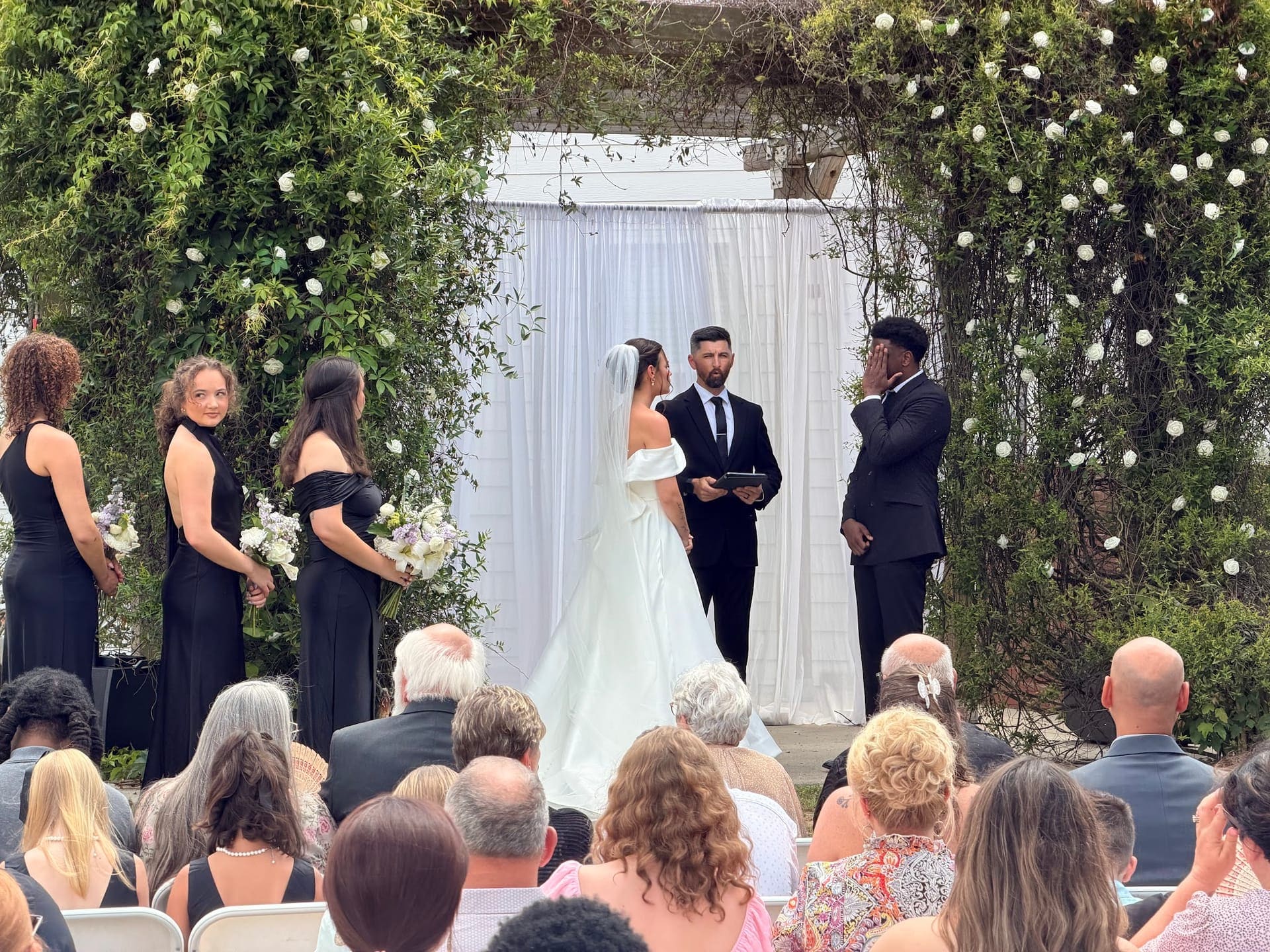 Wedding vows under a floral arch with guests at Scarborough House